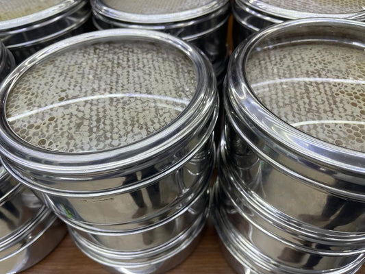 Stack of metal sieves with honeycomb patterns on a wooden surface